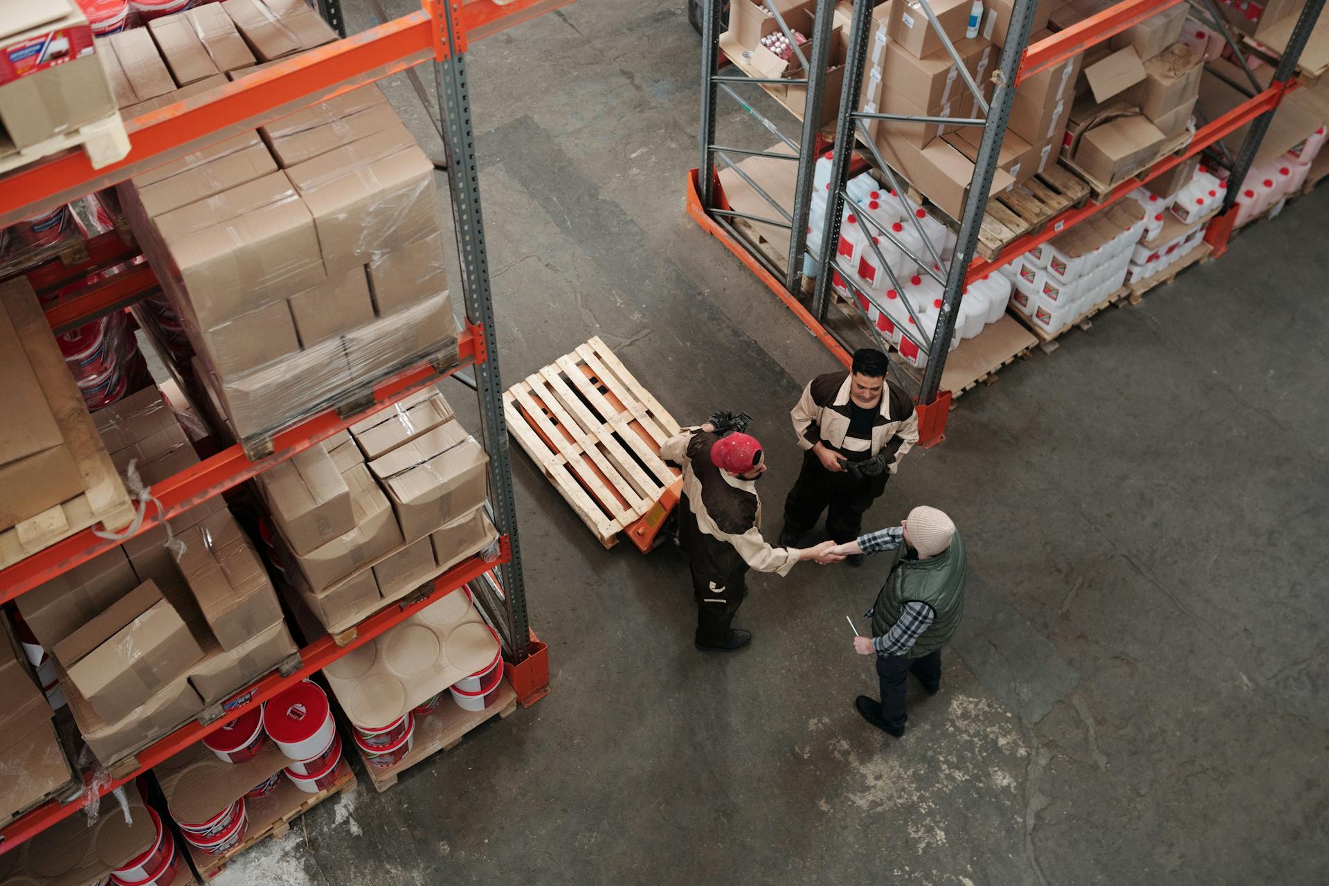 High-angle view of two business partners shaking hands inside a busy warehouse, representing product sourcing